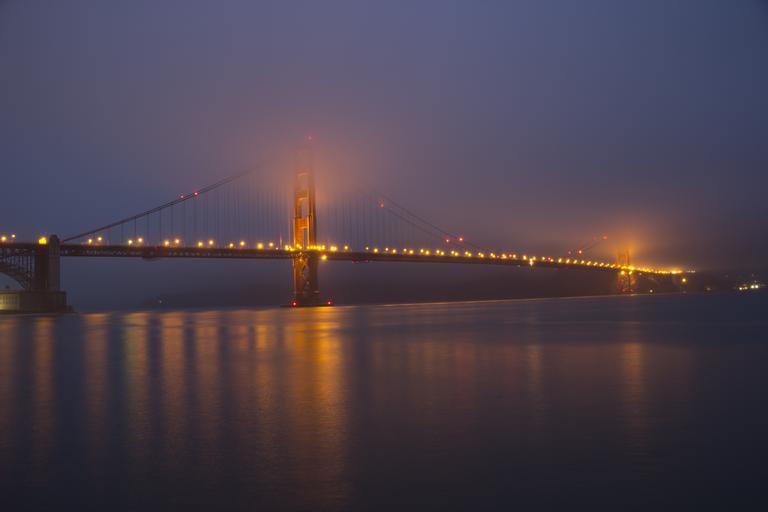 Photo of Golden Gate Bridge in San Francisco lit up at night with a misty sky